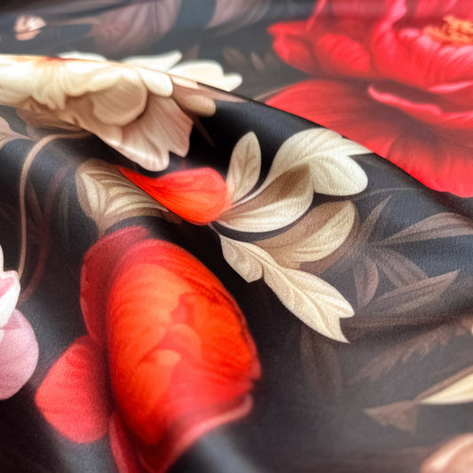Garden Glory – floral print on luxurious duchesse satin with bright red, orange, and cream flowers on a dark background, glossy surface and sculptural folds, design by Sewing Club.